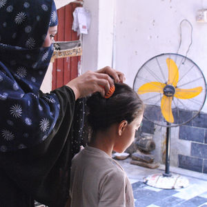 Zarghona Ali, who lives in Peshawar, Pakistan, puts her daughter's hair in a clip to keep her cooler on a hot day in July 2024. Credit: Saba Rehman