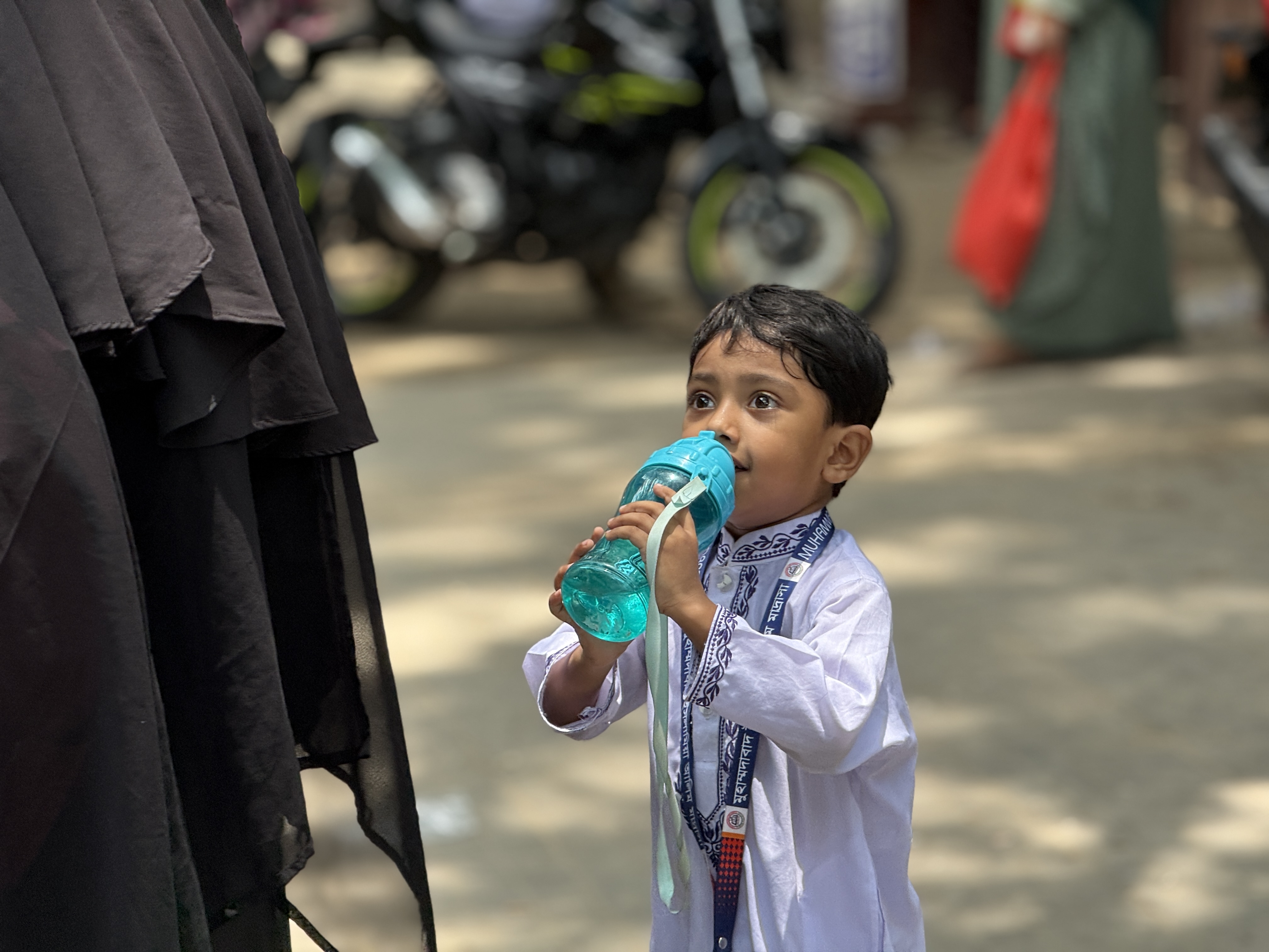 A young student drinks water after a hot school day in Dhaka, Bangladesh, as his mother looks for transport home for the pair, on May 29, 2025. Mosabber Hossain/Climate Resilience for All