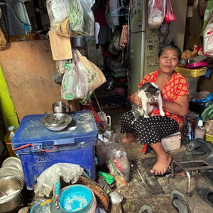 Somyong Ramieddee, 61, holds a pet cat while sitting near the doorway of her home in Khlong Toei, Bangkok, Oct. 10, 2025. Climate Resilience for All/Laurie Goering