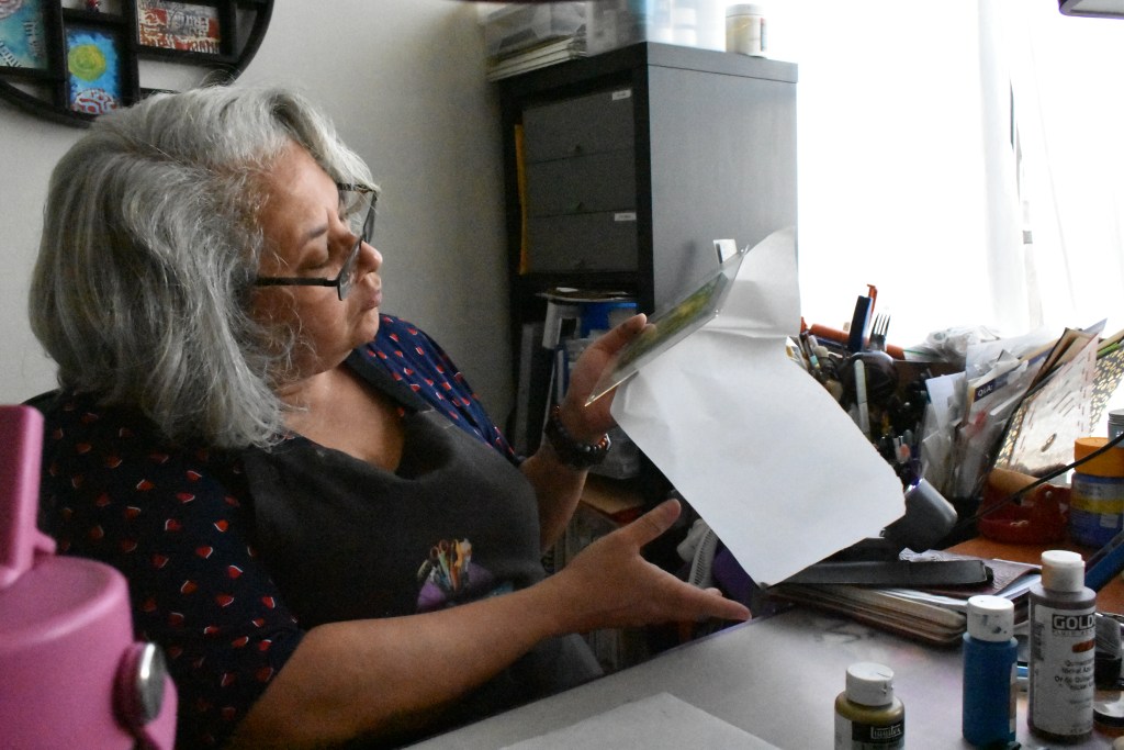 Home worker Estelle Banks examines a gel print prior to attempting a paper transfer before the paint dries in the dry, hot air at her desk, rendering the print useless, October 30, 2025. Climate Resilience for All/Rachel Parsons