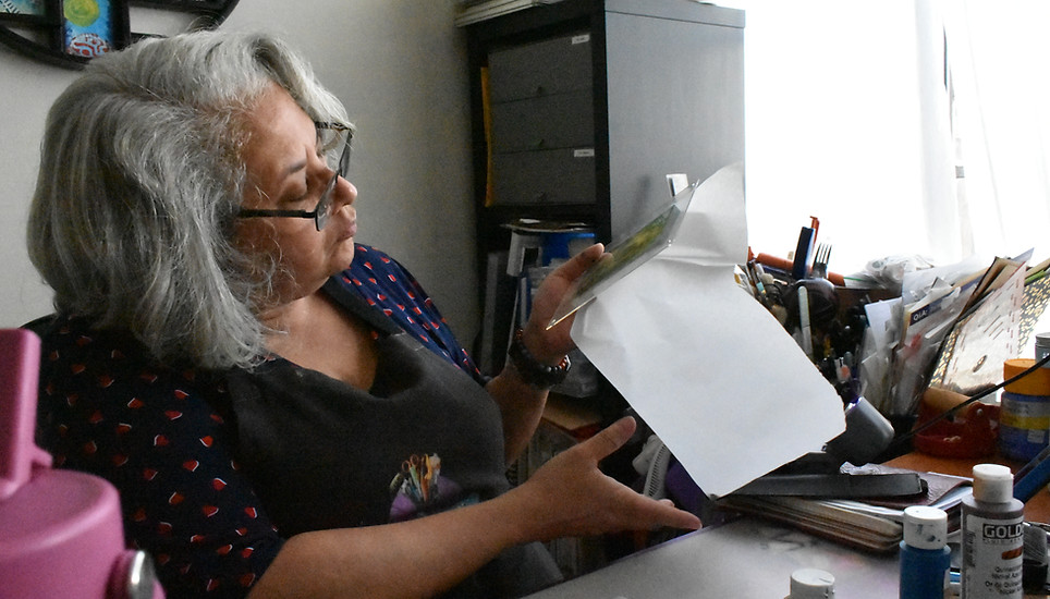 Home worker Estelle Banks examines a gel print prior to attempting a paper transfer before the paint dries in the dry, hot air at her desk, rendering the print useless, October 30, 2025. Climate Resilience for All/Rachel Parsons