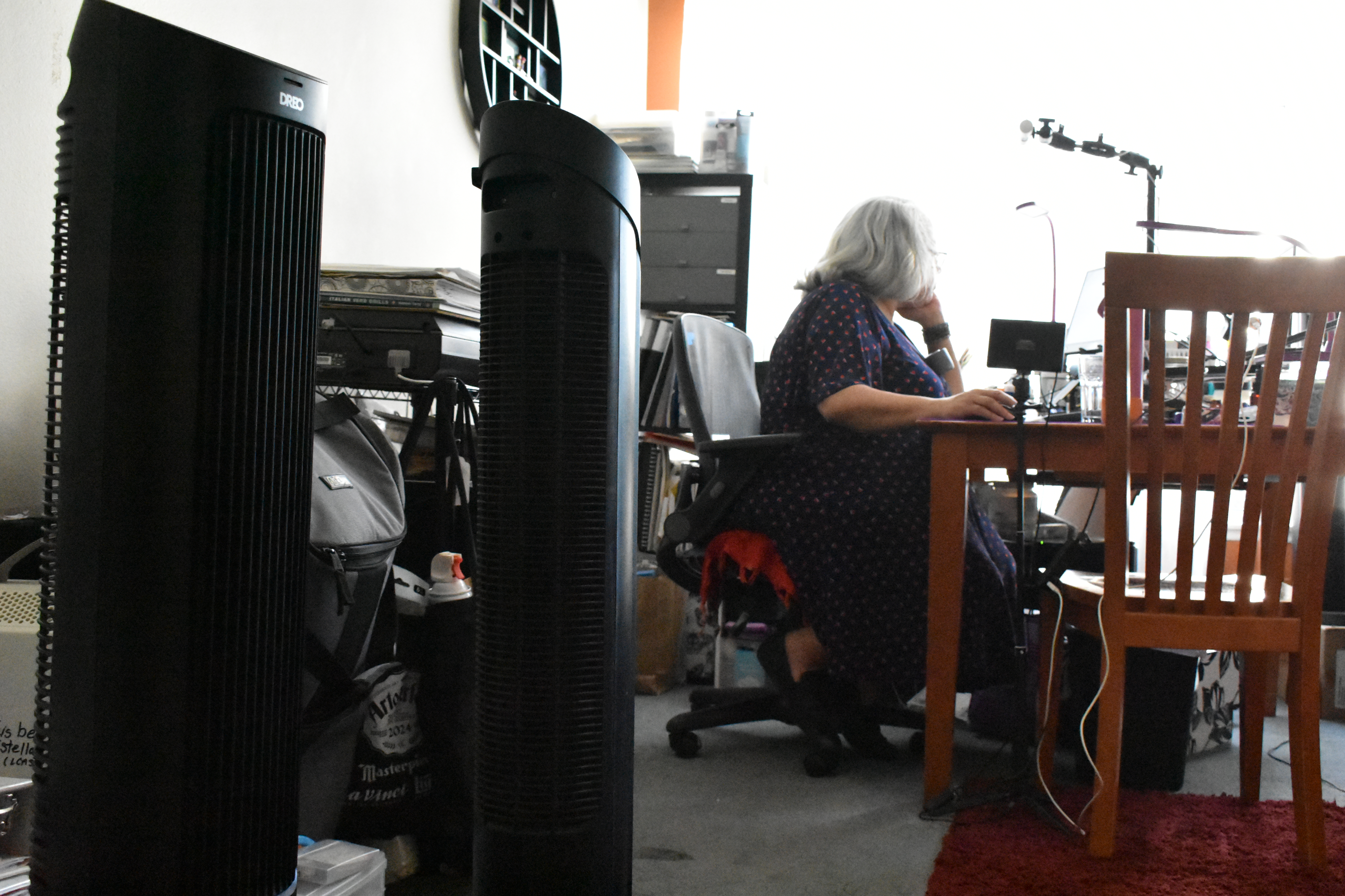 Estella Banks works at the desk in her home in Fullerton, California, on October 30, 2025. Two of her many electric fans move warm air around the room. Climate Resilience for All/Rachel Parsons