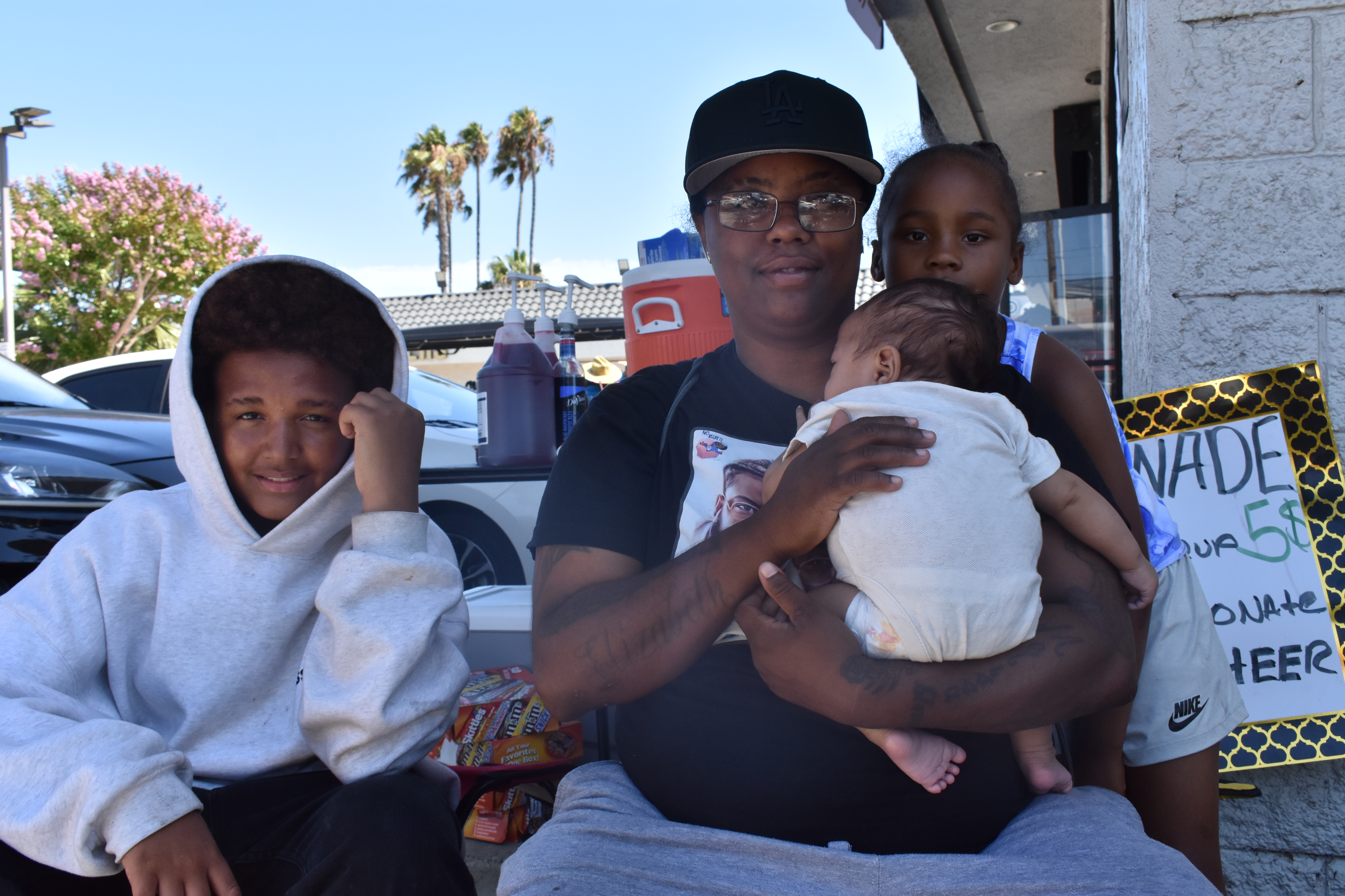 Street vendor Shay’Prea Moore, with her daughter and nephew, holds her youngest child while she waits for customers during L.A.’s World Cup opener on June 12, 2026. HERA/Rachel Parsons